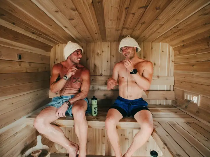 Two men sitting inside a barrel sauna, laughing