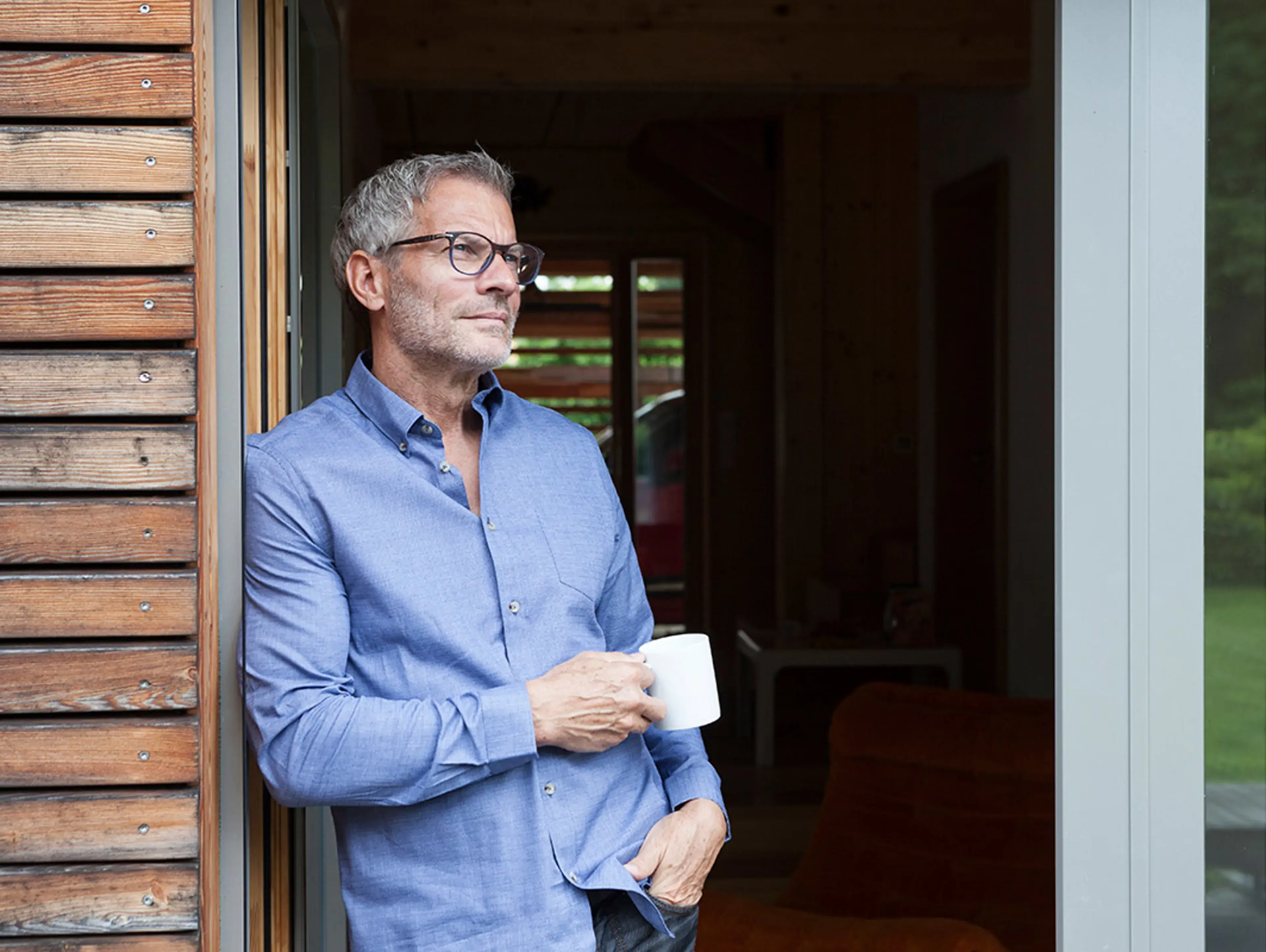 A man holding a mug in the doorway of a timber-clad building