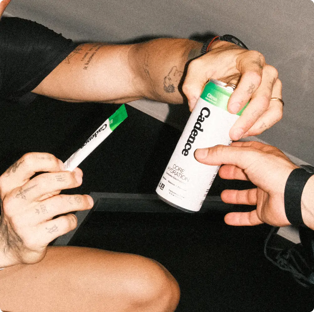 Hands tearing open a Cadence sachet over a bottle in a gym